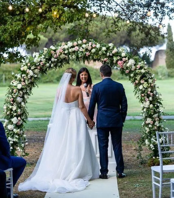 Your language is not on the list? Celebrant laughing with the couple under an arch of pink and white roses