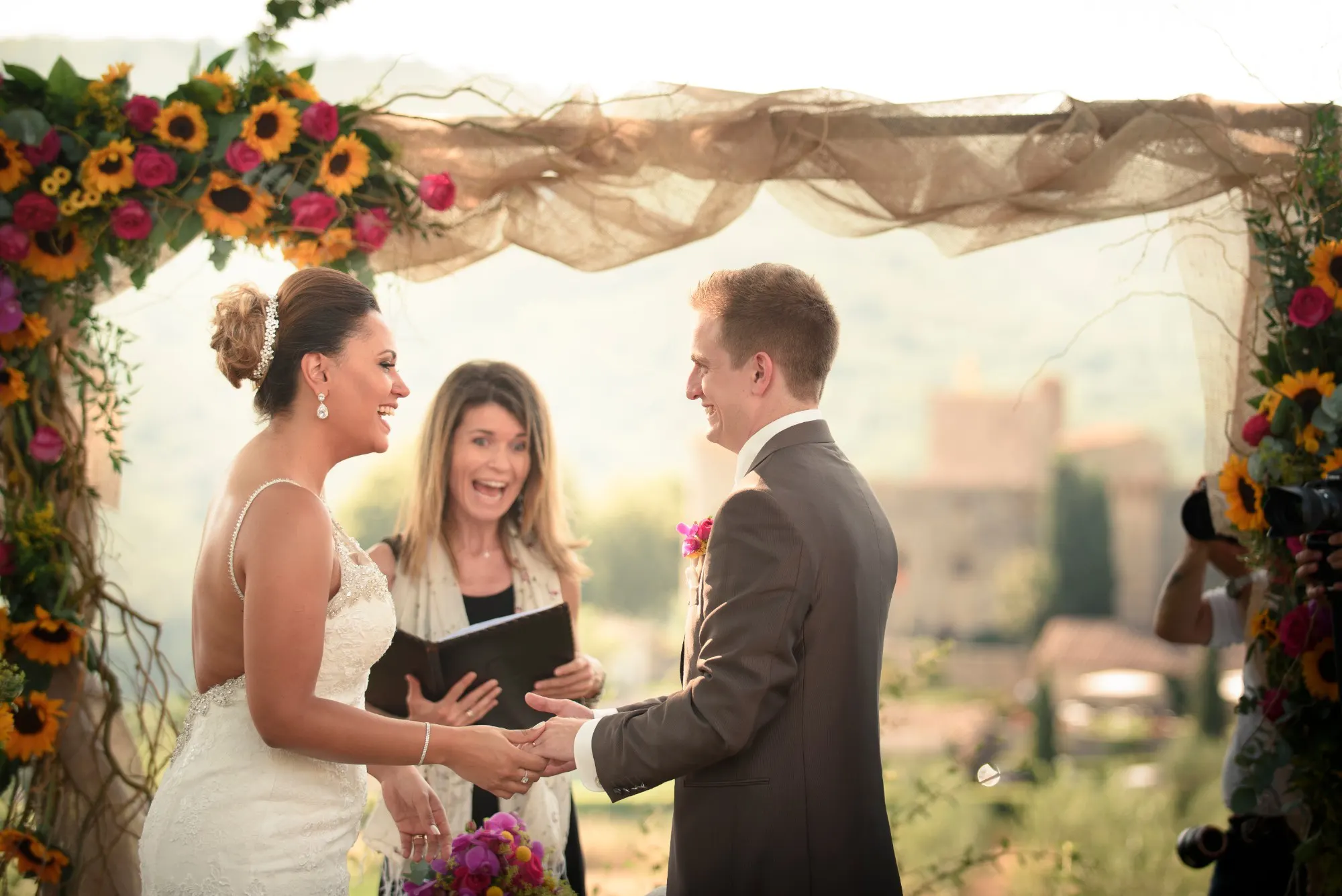 Celebrant laughing with the couple under a sunflower wedding arch in Tuscany Celebrant laughing with the couple under a sunflower wedding arch in Tuscany