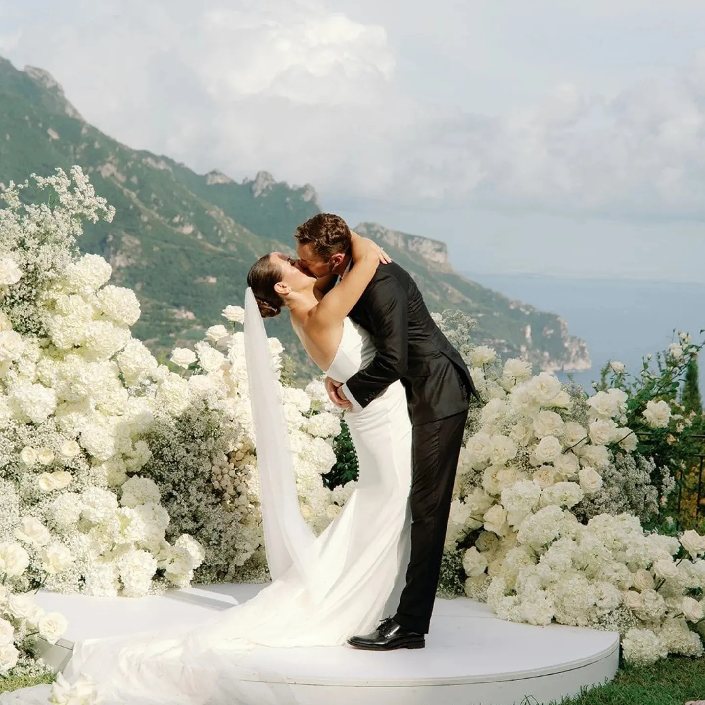 Photo: Kiran Dira Photography Couple kissing among white flowers with the Amalfi Coast behind them