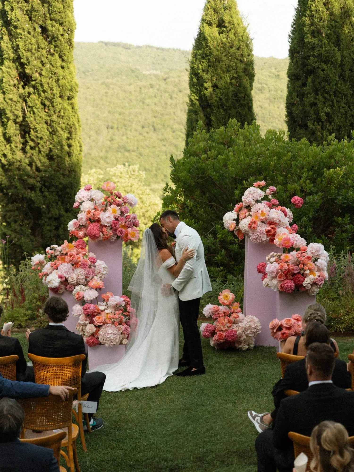 Foto: Photos by Gayle Sposi si baciano tra colonne di fiori rosa e cipressi alla fine della cerimonia