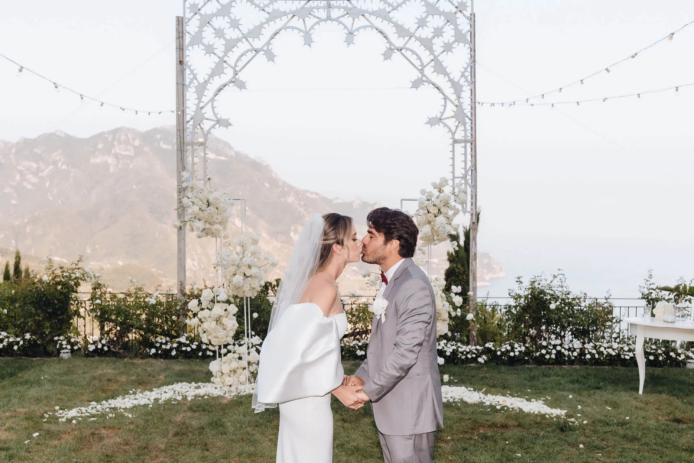Couple kissing under a white wedding arch with the Amalfi Coast mountains behind Couple kissing under a white wedding arch with the Amalfi Coast mountains behind