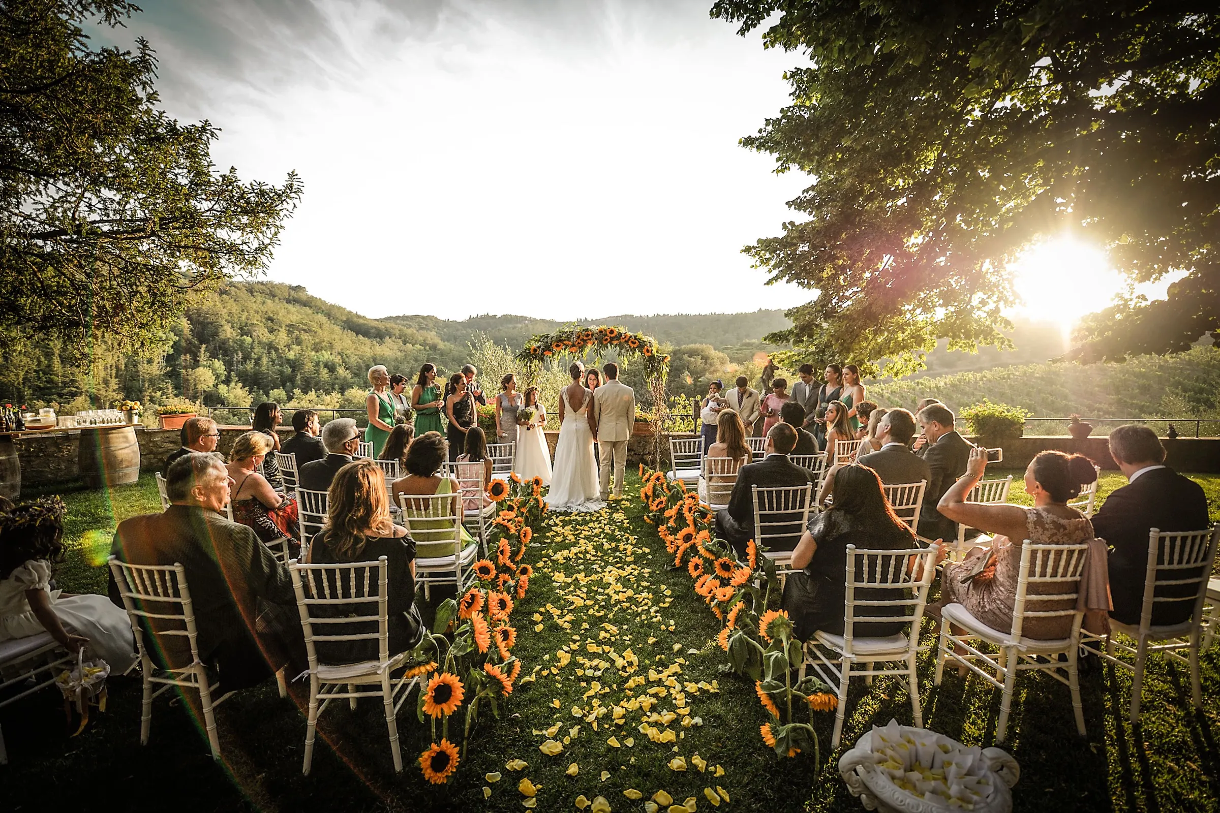 Wedding celebrants in Italy Guests seated along a sunflower aisle at a sunset wedding ceremony in the Tuscan hills